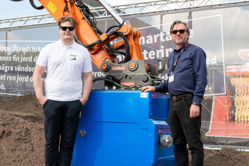 Amas Sales Support Vilgot Mäntynen (on the left), HRVB Hydraulic Recycling Vacuum Bucket (in the middle) and DYNASET Area Sales Manager Esa Kannisto in Maskinmässan 2022 at Stockholm, Sweden.